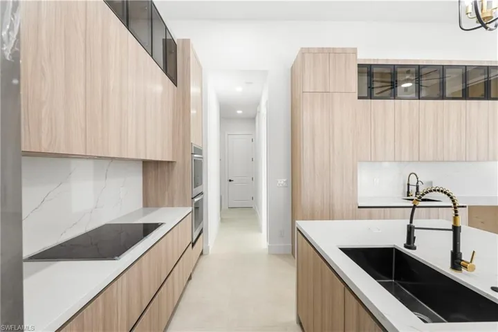 Contemporary kitchen featuring light wood-finish cabinetry, white countertops, and a full-height white backsplash with subtle veining