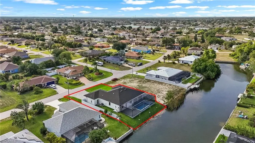 Canal-front property featuring a screened-in pool area and lush green landscaping