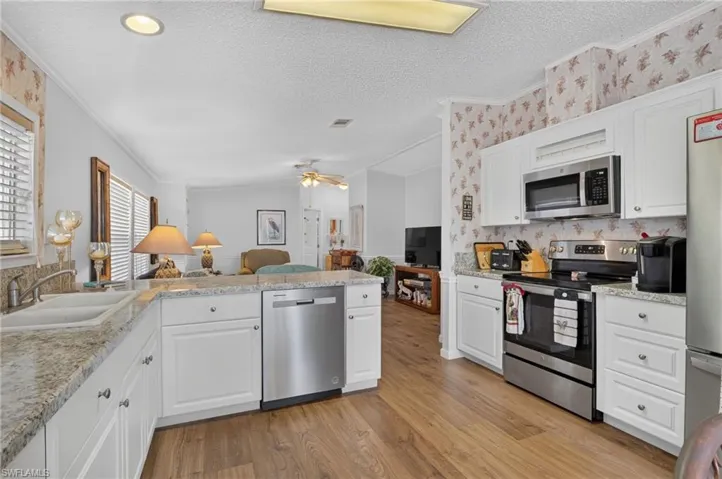 Kitchen featuring white cabinetry, stainless steel appliances, a double basin sink, light-toned countertops, and wood-finish flooring