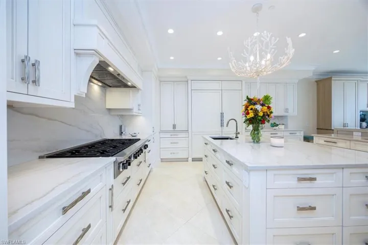 Kitchen with white cabinetry, light stone countertops, a kitchen island with sink, and decorative light fixtures