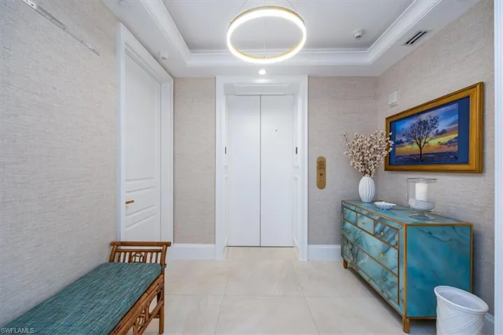 Hall with a raised ceiling, elevator, and light tile patterned floors