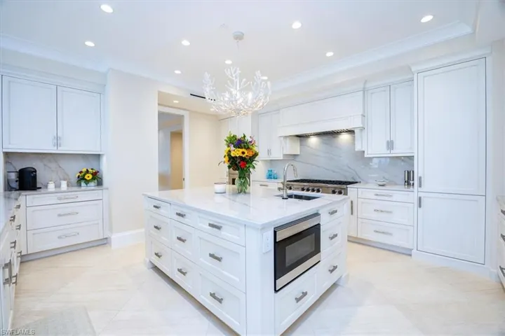 Kitchen with a kitchen island with sink, backsplash, hanging light fixtures, appliances with stainless steel finishes, and white cabinetry