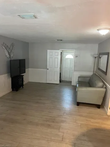 Living room with visible vents, light wood-type flooring, and a wainscoted wall