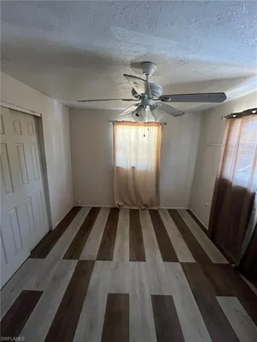 Empty room with wood finished floors, ceiling fan, and a textured ceiling