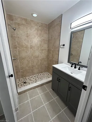 Bathroom featuring tiled shower, vanity, and tile patterned flooring