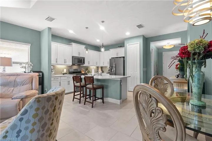 Open-concept kitchen featuring white cabinetry, stainless steel appliances, a center island with seating, and light-toned tile flooring