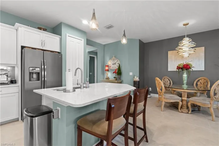 Kitchen island featuring a white countertop with integrated sink and chrome faucet, under-cabinet storage, and pendant lighting