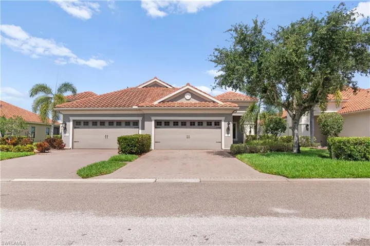 Tile roof residence featuring a two-car garage, paver driveway, mature landscaping, and stucco exterior finish