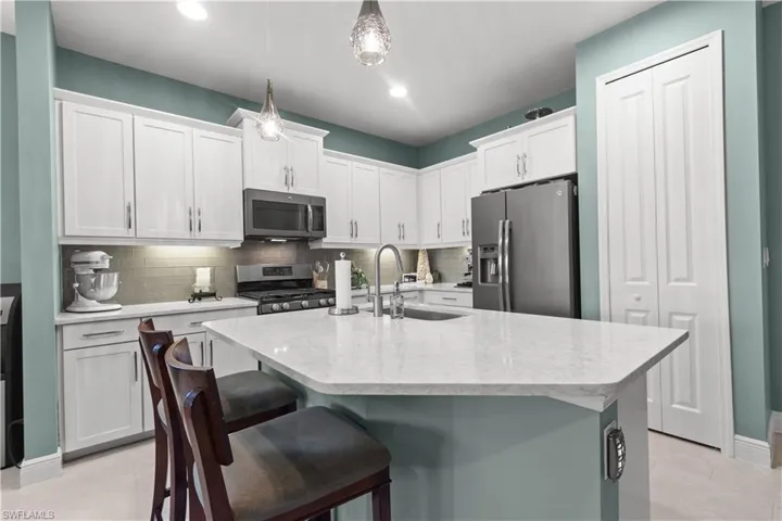 Modern kitchen featuring white shaker cabinetry, stainless steel appliances, a light-toned countertop, and a tile backsplash