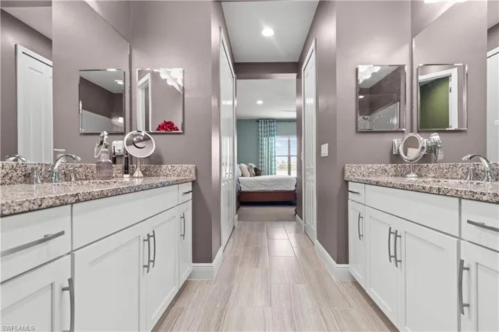 Primary bathroom featuring dual white vanities with granite countertops, undermount sinks, chrome fixtures, and wood-finish tile flooring