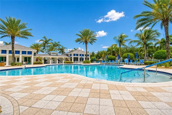 Expansive pool area featuring a large swimming pool, patterned paver deck, and lush tropical landscaping