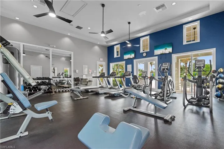 Spacious fitness center featuring various exercise machines, strength training equipment, large windows, ceiling fans, and recessed lighting