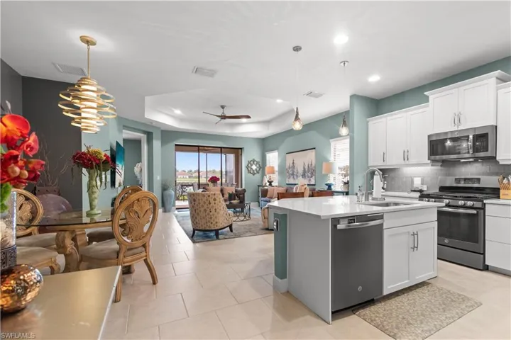 Open concept living space featuring a modern kitchen island with an integrated dishwasher, white shaker cabinetry, stainless steel appliances, and a tiled backsplash