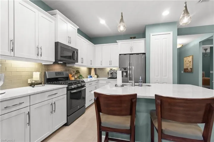 Kitchen featuring white shaker-style cabinetry, light-toned countertops, subway tile backsplash, and stainless steel appliances