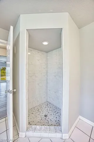 Primary Bathroom with tile patterned flooring, a shower stall, baseboards, and a textured ceiling