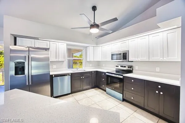 Kitchen with stainless steel appliances, a sink, vaulted ceiling, ceiling fan, and light tile patterned floors
