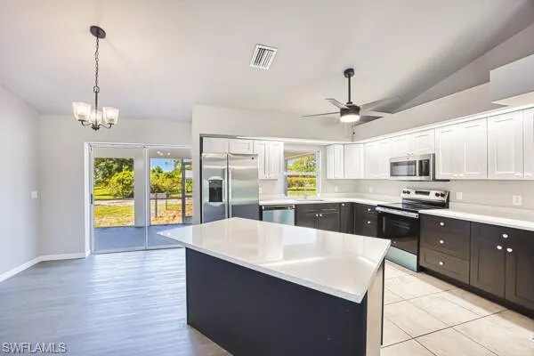 Kitchen featuring appliances with stainless steel finishes, white cabinets, light countertops, decorative light fixtures, and a chandelier