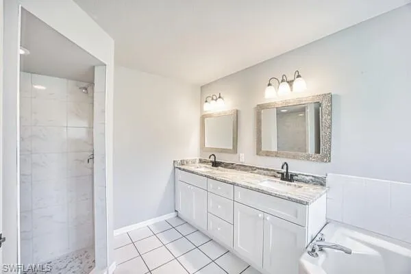 Primary bathroom featuring tiled shower, double vanity, a garden tub, tile patterned floors, and baseboards