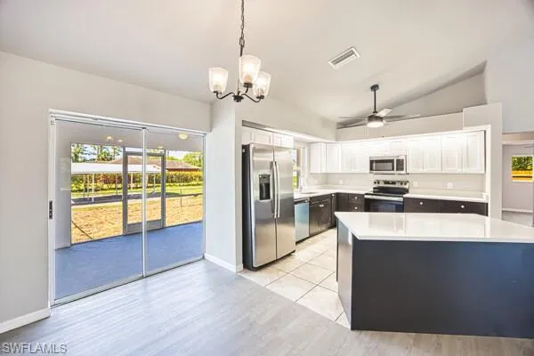 Kitchen with appliances with stainless steel finishes, light countertops, vaulted ceiling, ceiling fan, and a chandelier