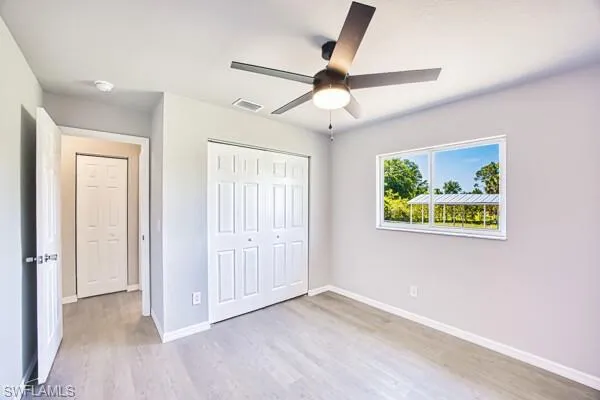 Unfurnished bedroom with wood finished floors, a closet, baseboards, and a ceiling fan