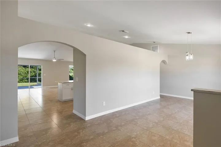 Empty room with lofted ceiling, light tile patterned floors, and ceiling fan