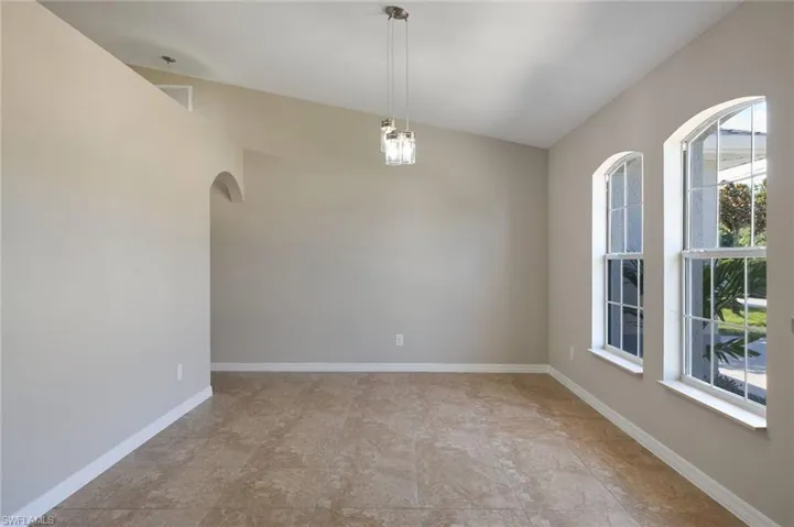 Empty room featuring light tile patterned flooring, a wealth of natural light, and vaulted ceiling