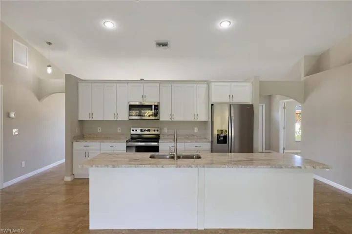 Kitchen with light tile patterned flooring, stainless steel appliances, a kitchen island with sink, and sink