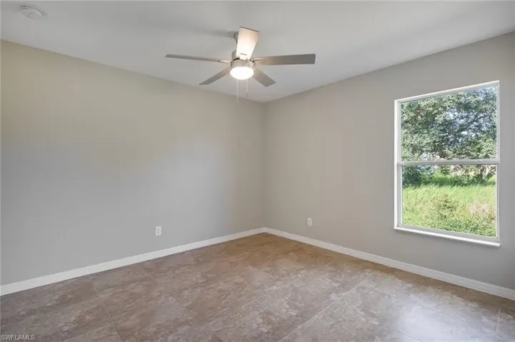 Tiled spare room featuring a wealth of natural light and ceiling fan
