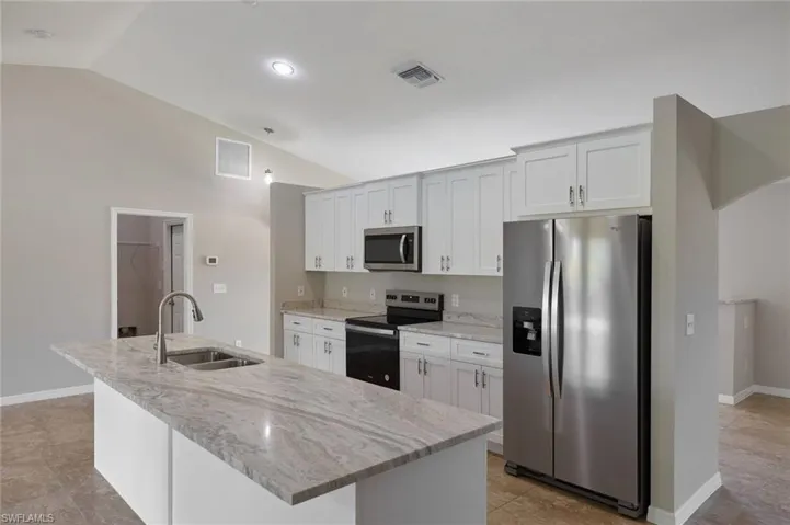 Kitchen with stainless steel appliances, vaulted ceiling, white cabinets, sink, and a kitchen island with sink