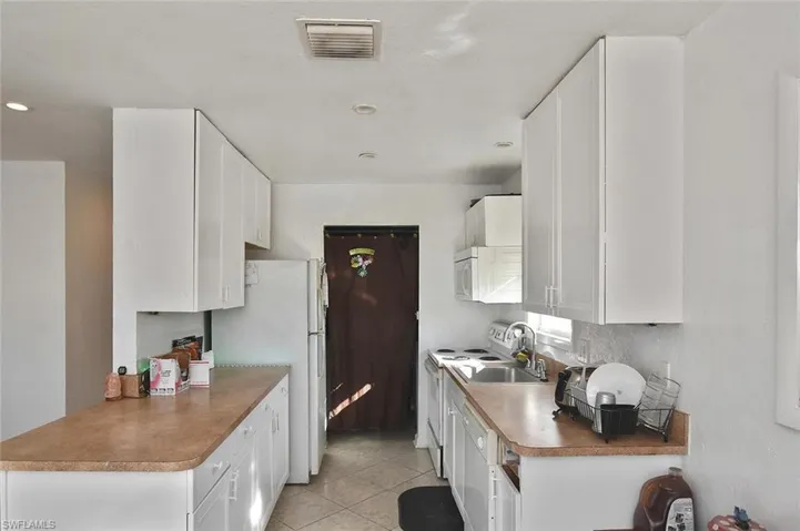 Kitchen featuring white cabinetry, white appliances, and light tile patterned flooring