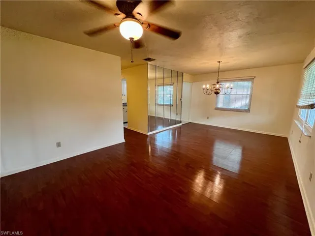Unfurnished room with dark wood-type flooring and ceiling fan with notable chandelier
