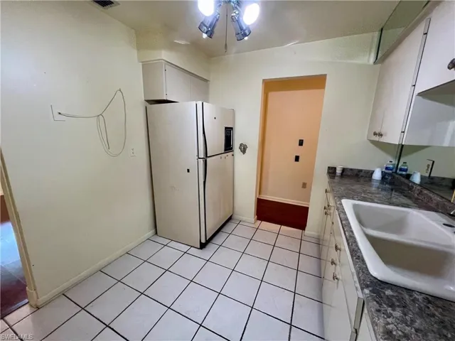 Kitchen featuring light tile flooring, white fridge with ice dispenser, ceiling fan, white cabinetry, and sink