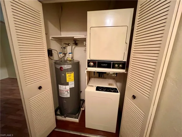Laundry area featuring water heater, stacked washer / drying machine, and dark hardwood / wood-style flooring