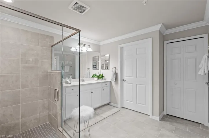 Bathroom featuring vanity, crown molding, a shower stall, visible vents, and a closet