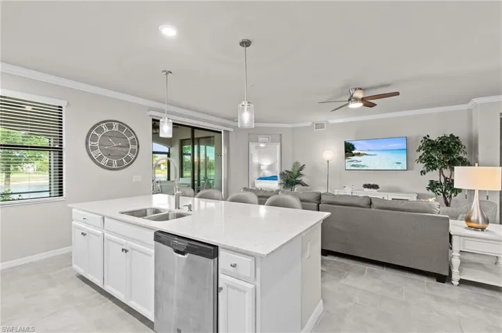 Kitchen featuring open floor plan, ornamental molding, stainless steel dishwasher, a sink, and white cabinets