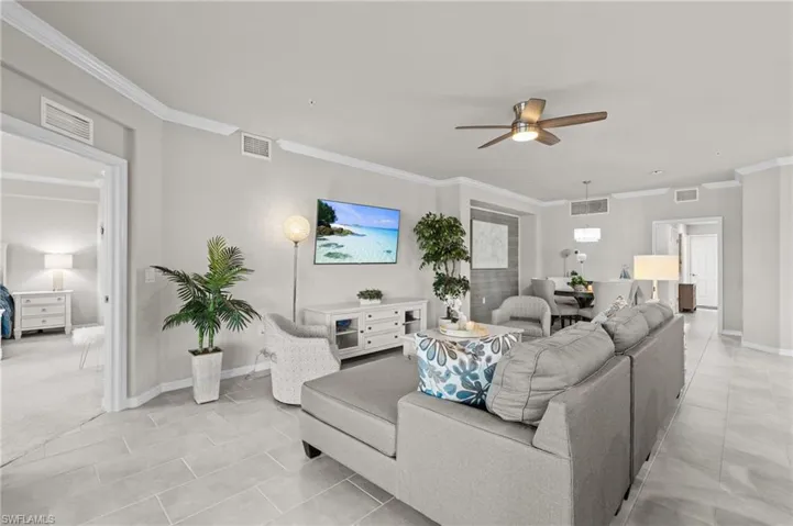 Living room with a ceiling fan, ornamental molding, and visible vents