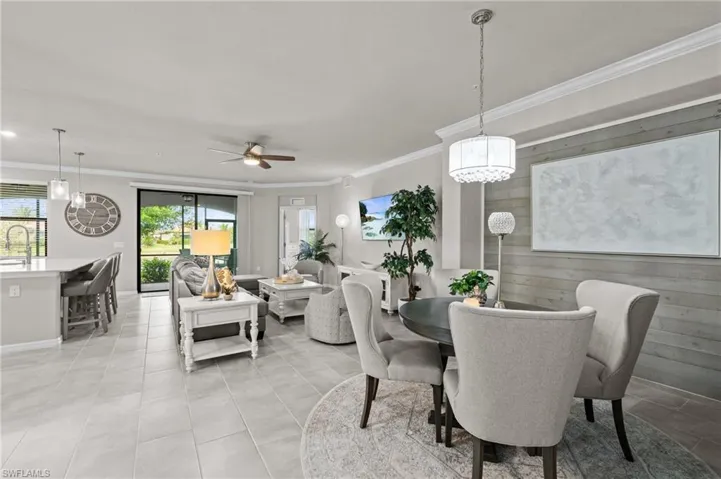 Dining space featuring light tile patterned flooring, ornamental molding, ceiling fan with notable chandelier, and wooden walls