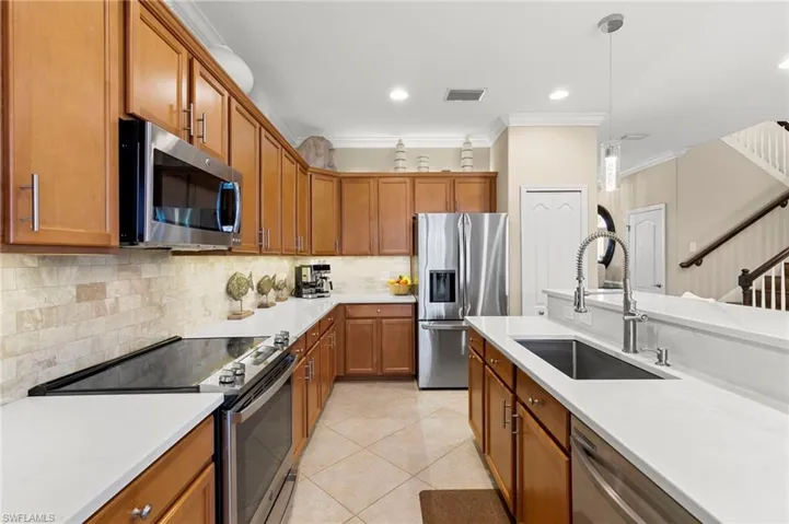 Kitchen featuring appliances with stainless steel finishes, brown cabinets, crown molding, hanging light fixtures, and light stone counters