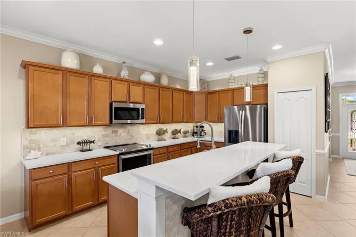 Kitchen with brown cabinets, light tile patterned floors, stainless steel appliances, crown molding, and pendant lighting