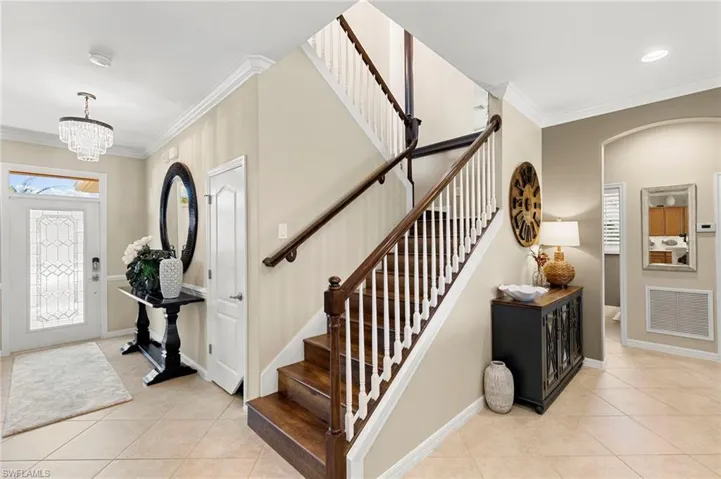 Entryway with ornamental molding, light tile patterned floors, a chandelier, arched walkways, and stairs