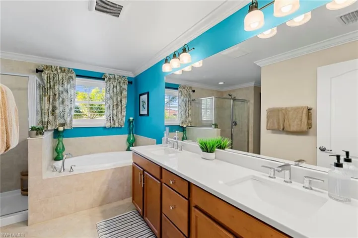 Bathroom with a stall shower, double vanity, light tile patterned floors, a garden tub, and crown molding