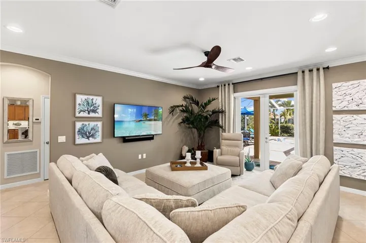 Living area featuring light tile patterned floors, recessed lighting, ceiling fan, crown molding, and arched walkways