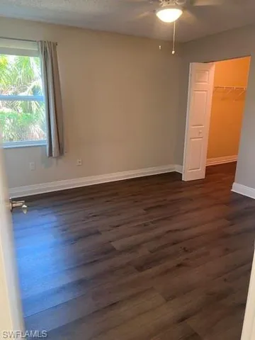 Unfurnished bedroom featuring a spacious closet, ceiling fan, dark wood-style flooring, and a textured ceiling