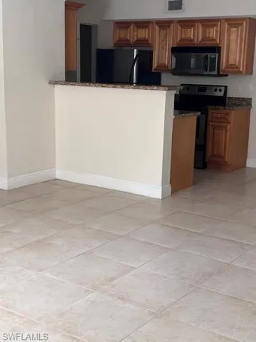 Kitchen with black appliances, wood finish cabinetry, dark stone countertops, and light tile patterned flooring