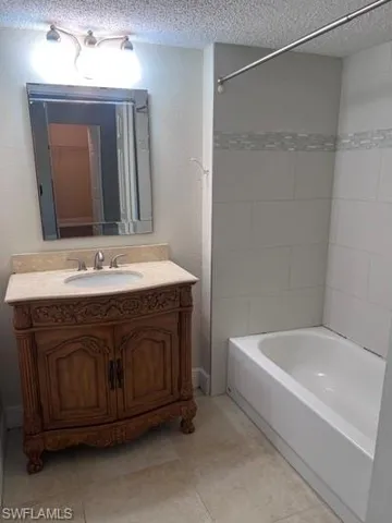 Bathroom with vanity, a textured wall, a textured ceiling, and shower / bath combination