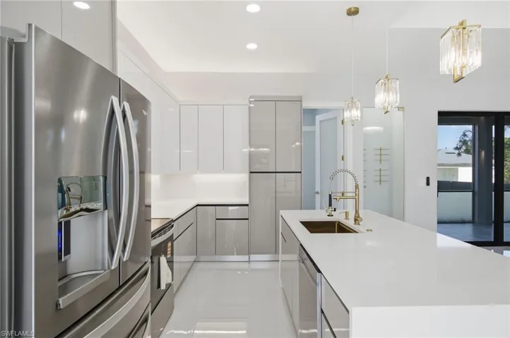 Kitchen featuring stainless steel appliances, modern cabinets, a center island with sink, hanging light fixtures, and white cabinets