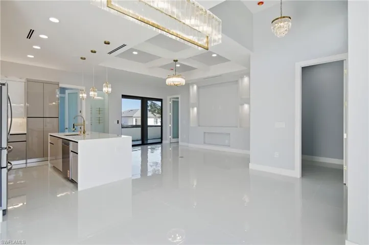 Kitchen with a chandelier, a kitchen island with sink, pendant lighting, coffered ceiling, and light stone counters