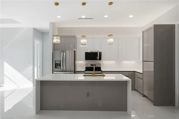 Kitchen featuring modern cabinets, white cabinetry, stainless steel appliances, pendant lighting, and a kitchen island with sink