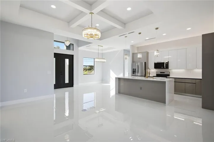 Kitchen featuring coffered ceiling, white cabinets, hanging light fixtures, a center island with sink, and beamed ceiling