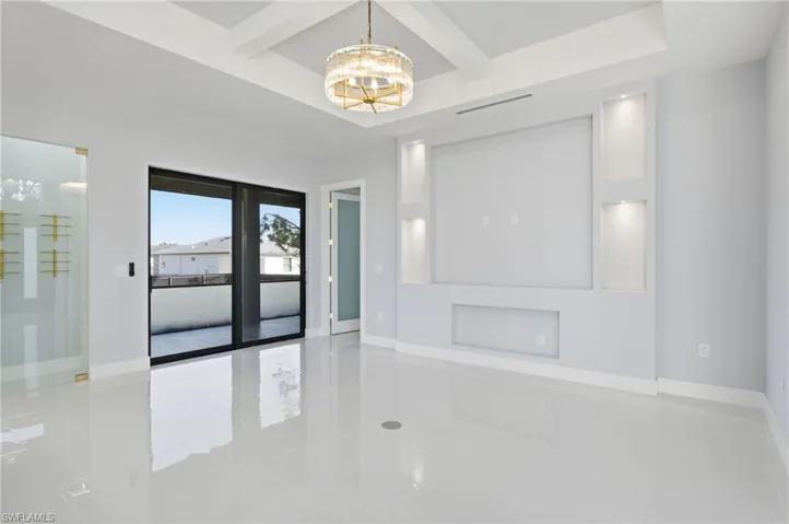 Empty room featuring coffered ceiling, beam ceiling, a chandelier, and light tile patterned flooring